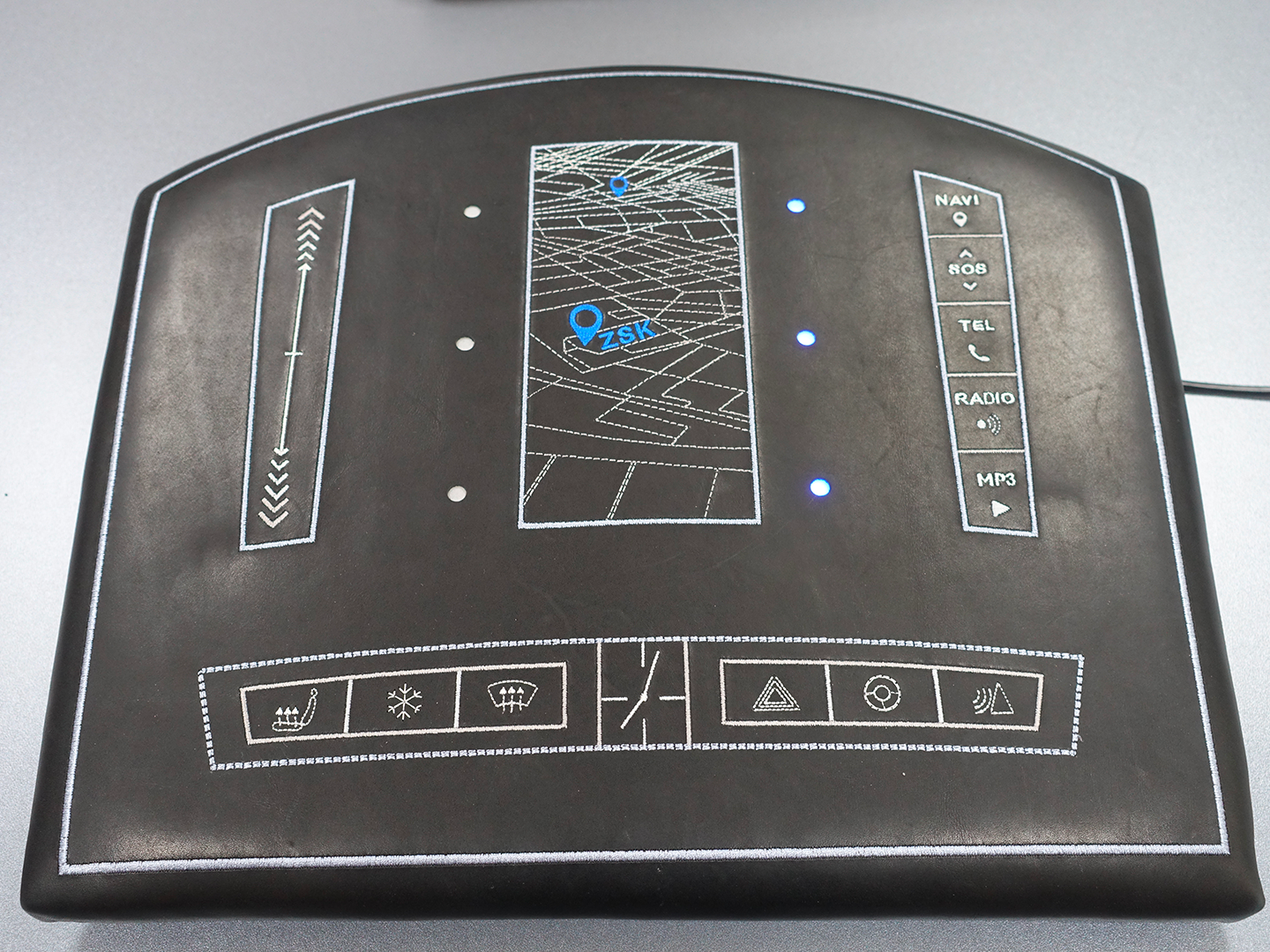 3E Smart Dashboard - Smart textiles demonstrator, consisting of a ZSK E-Textiles Board, six ZSK LED Sequins, three embroidered capacitive touch sensors and one embroidered capacitive touch slider to control the LEDs. The embroidered functional layer is covered by a decorative layer of padded leather.