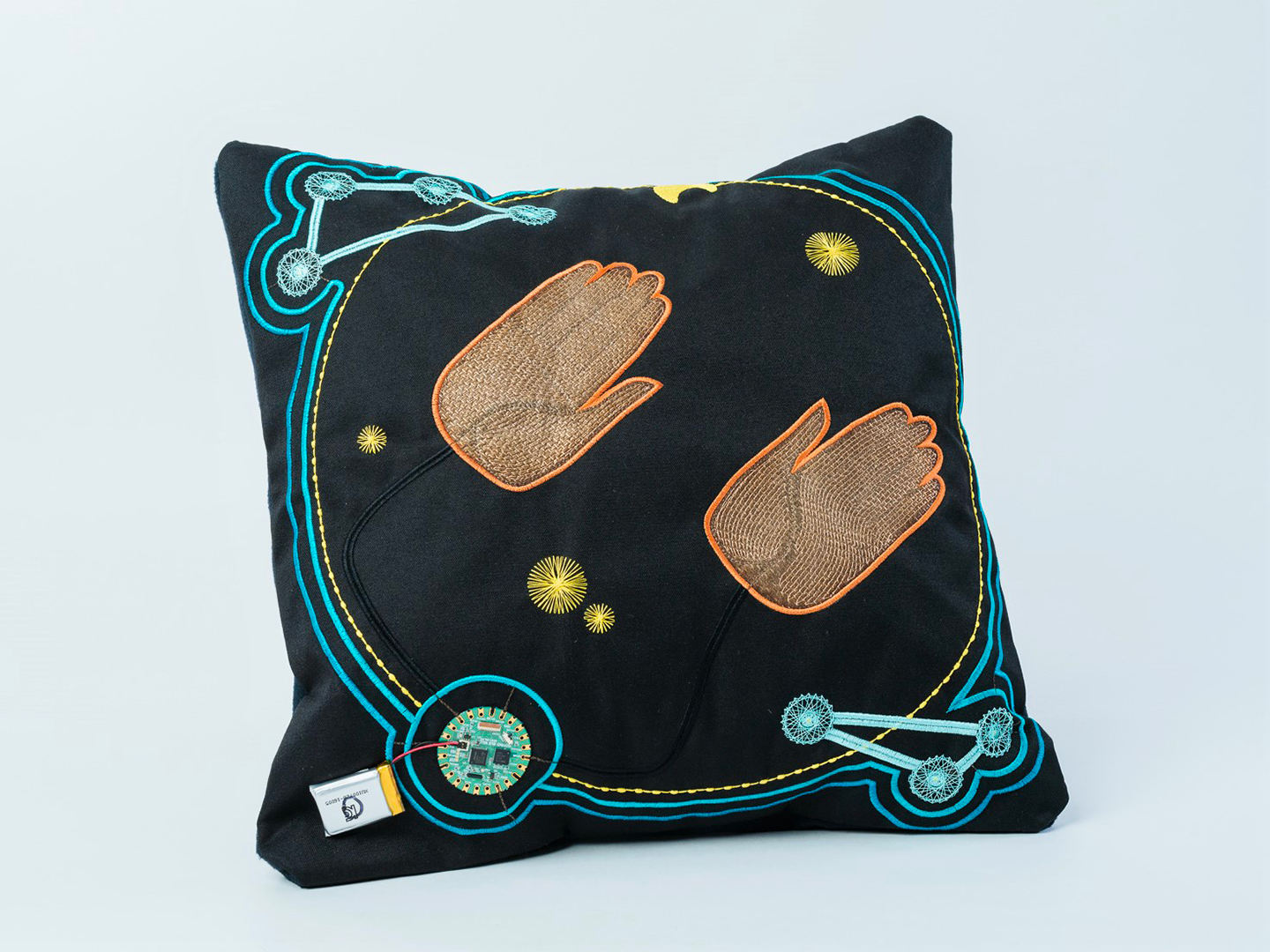 3E Smart Pillow - Smart textiles demonstrator, consisting of a PCB, six ZSK LED Sequins and two embroidered hand-shaped capacitive touch sensors to control the LEDs.